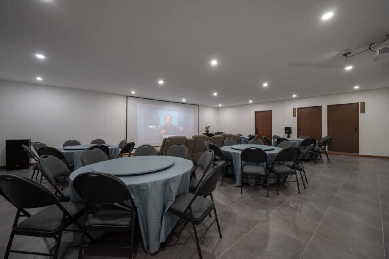 Un salón de conferencias con varias mesas y sillas, una pantalla de proyector y un orador.