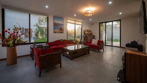 Un salón amplio con un sofá rojo, una mesa de centro y un televisor. Hay ventanas grandes y vistas al exterior.