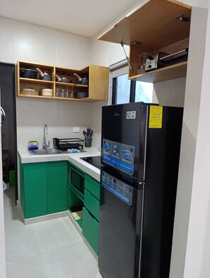 Eine kompakte Küche mit schwarzem Kühlschrank, grünen Schränken, einem eingebauten Backofen und einem Fenster über der Spüle.