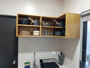 Eine Küche mit einer Holzwandregal, die Kochgeschirr trägt, einem Spülbecken mit Wasserhahn und einem Geschirrgestell.