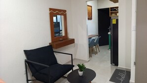 A modern living room with a black armchair, a small round table with a plant, a mirror, and a doorway leading to a dining area. - Loft moderno norte | Ideal parejas/trabajo (Merida)