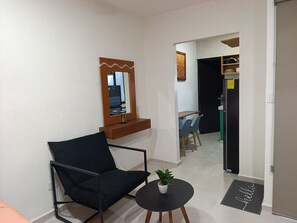 Ein modernes Wohnzimmer mit einem schwarzen Sessel, einem kleinen runden Tisch mit einer Pflanze, einem Spiegel und einer Tür zu einem Essbereich.