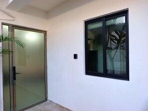 Un couloir avec une porte-fenêtre coulissante, une petite fenêtre donnant sur des plantes et un interrupteur sur le mur.