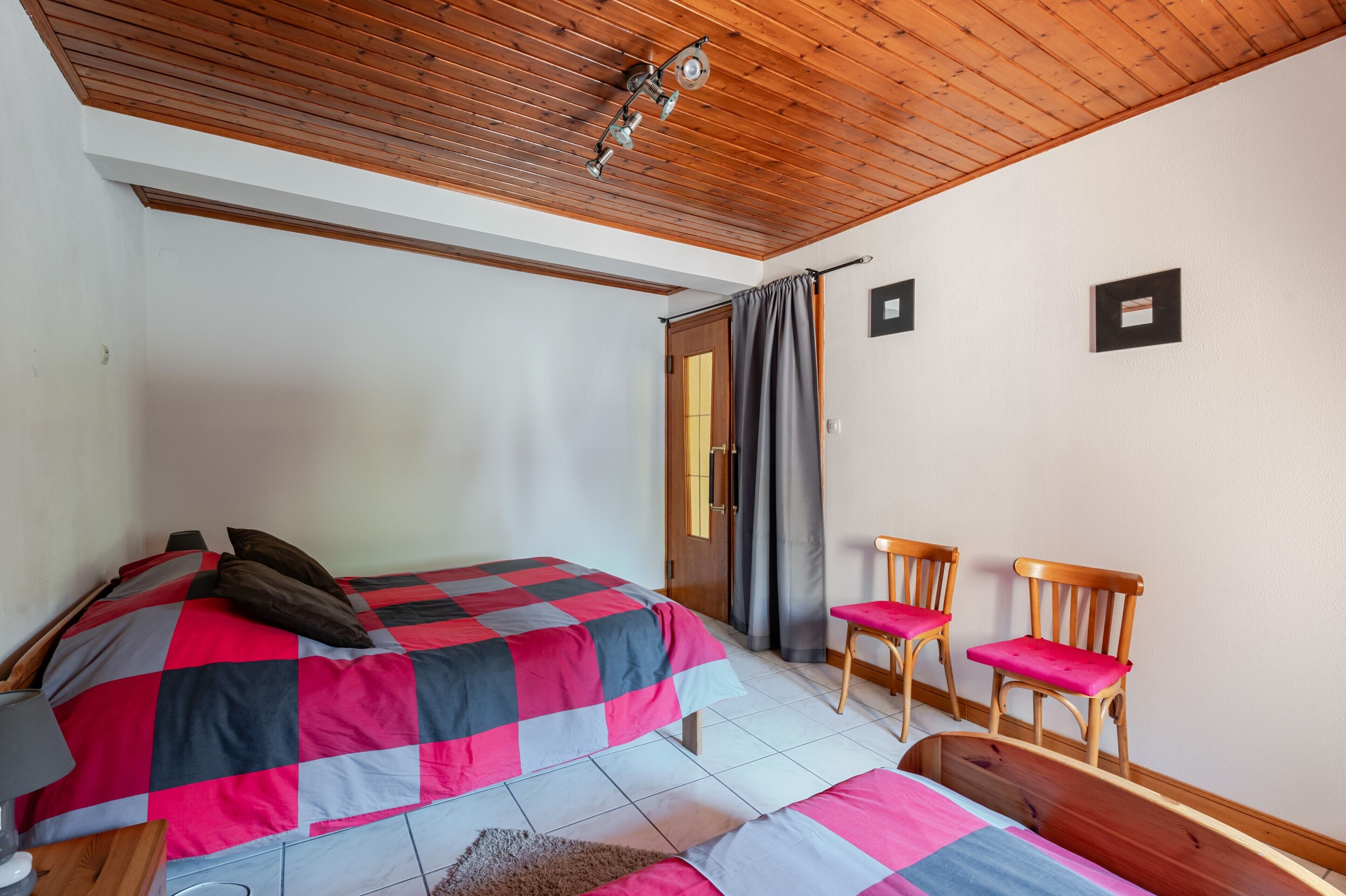 A bedroom with a bed, two chairs, a wooden ceiling, and a door.