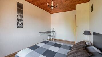 A bedroom with a bed, a desk, a chair, a lamp, and a cityscape artwork on the wall.