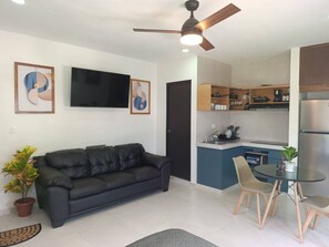 Ein modernes Wohnzimmer mit einer schwarzen Ledersofa, einem Esstisch mit Stühlen, einer Küchenzeile und einem Deckenventilator.