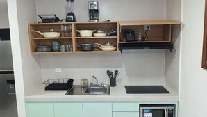 Una cocina con microondas, pileta y diversos utensilios en estantes.