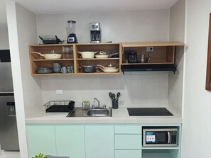 Una cucina con forno a microonde, lavandino e diversi utensili sugli scaffali.