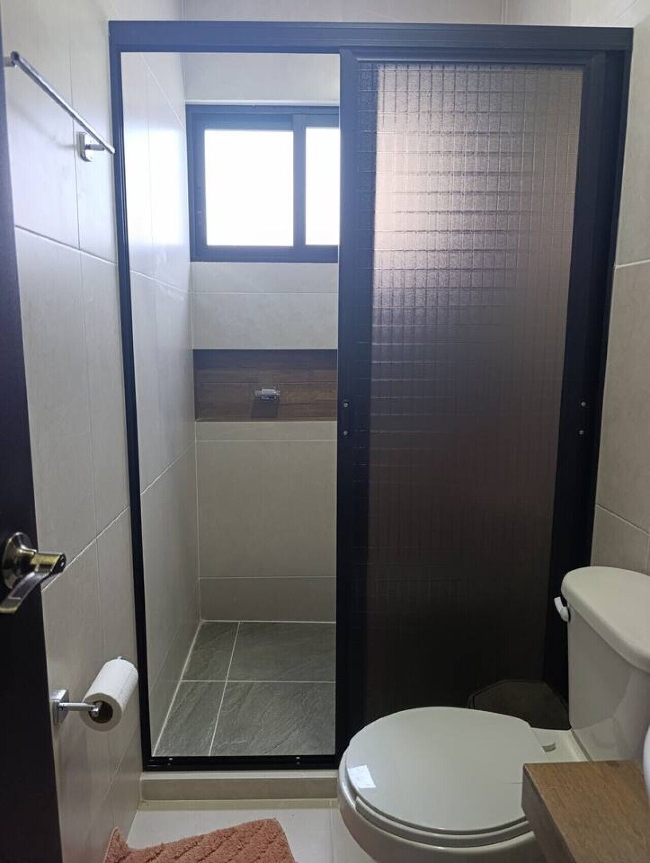 A bathroom with a shower, toilet, and a towel rack.
