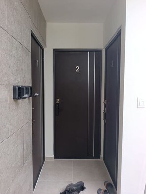Une entrée moderne avec une porte sombre portant le numéro 2, un sol carrelé et une paire de chaussures posées sur le sol.