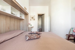 A bedroom with a bed, pillows, a wooden headboard, a bedside table, a mirror, and a door leading to a bathroom. - B&B Girasole - Camera Matrimoniale (Gallipoli)