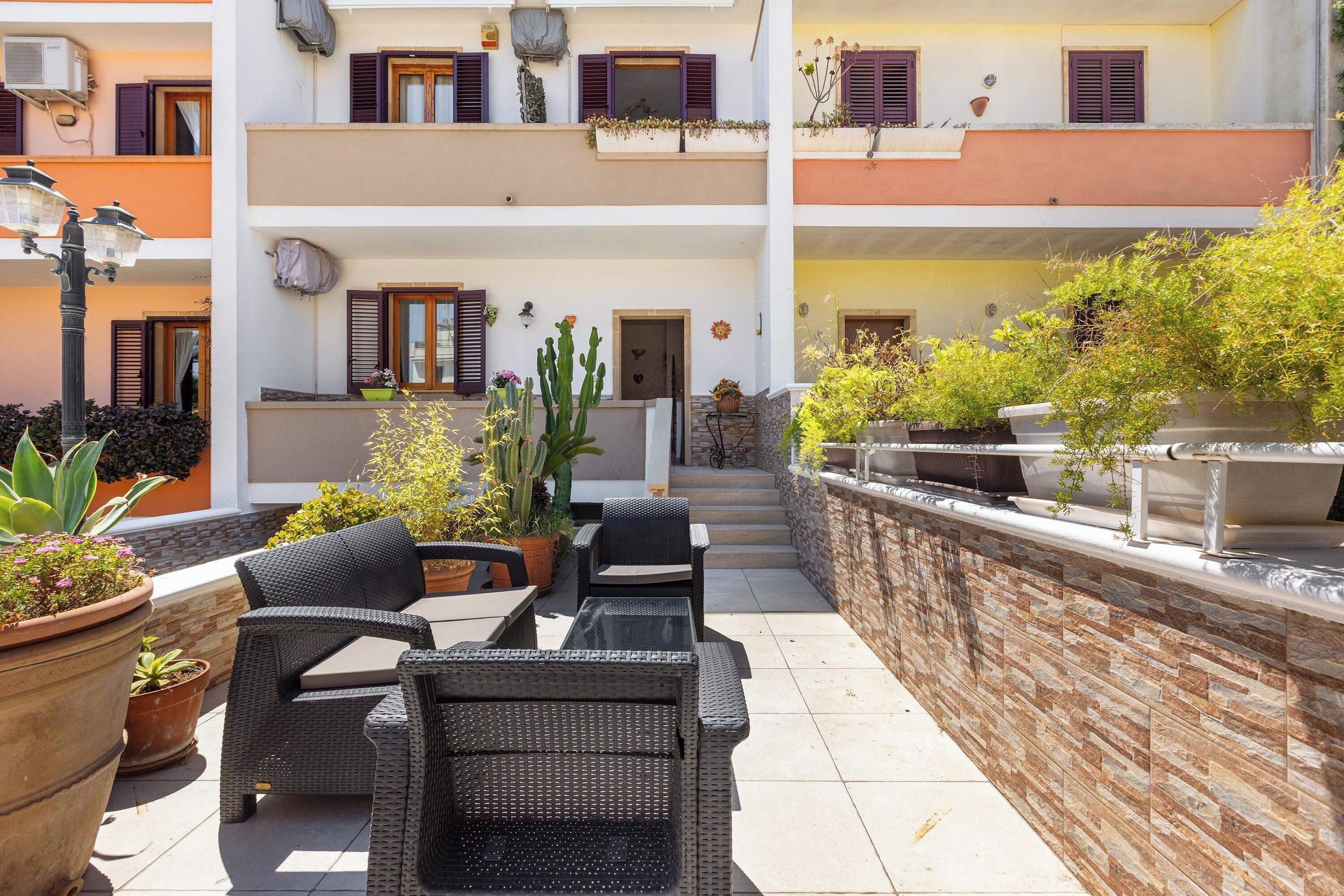 A courtyard with wicker furniture, potted plants, and a stone wall.