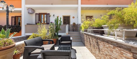 A courtyard with wicker furniture, potted plants, and a stone wall.