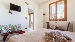 Quarto com uma cama, televisão, janela e porta que dá para outro cômodo.