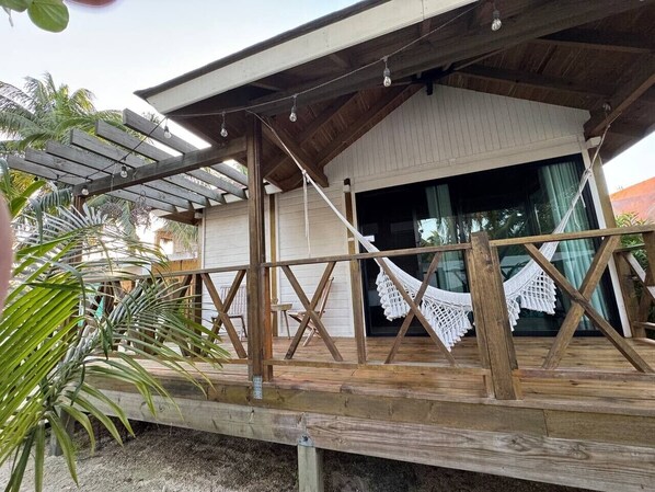 A wooden deck with a hammock, a pergola with string lights, and a building with a large window.