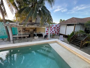 A swimming pool with a concrete deck, a small outdoor kitchen area, and a covered seating area with a red pattern wall.