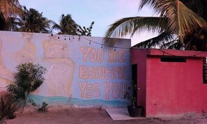 A wall with a mural that says 'YOU ARE BEAUTIFUL YES YOU' and a red building adjacent to it.