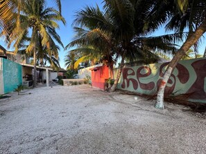A sandy outdoor area with palm trees, a red building, and a wall with a mural.