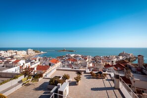 Paisagem costeira com vista para o mar, edifícios com telhados vermelhos e céu claro.