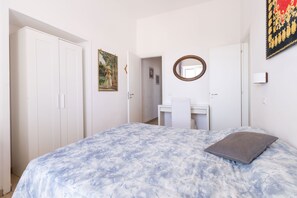 Ein Schlafzimmer mit Bett, Schrank, Schreibtisch, Spiegel und einem Bild an der Wand.