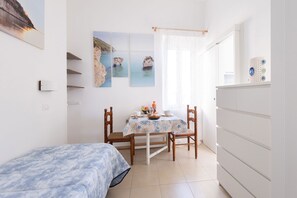 Une chambre à coucher comprenant un lit, une table avec des chaises, une commode et des œuvres d’art murales.