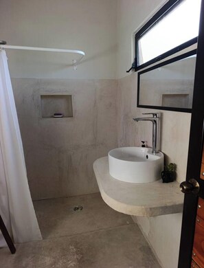 Une salle de bain avec un lavabo blanc, un miroir, une douche et une petite étagère.