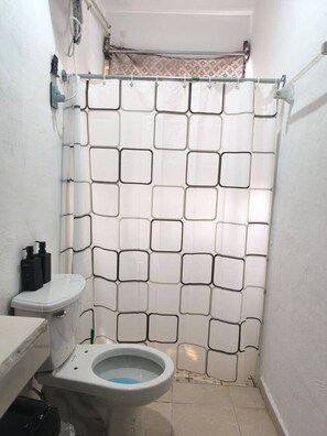 Een kleine badkamer met toilet, wastafel en douchegordijn met een geometrisch patroon.