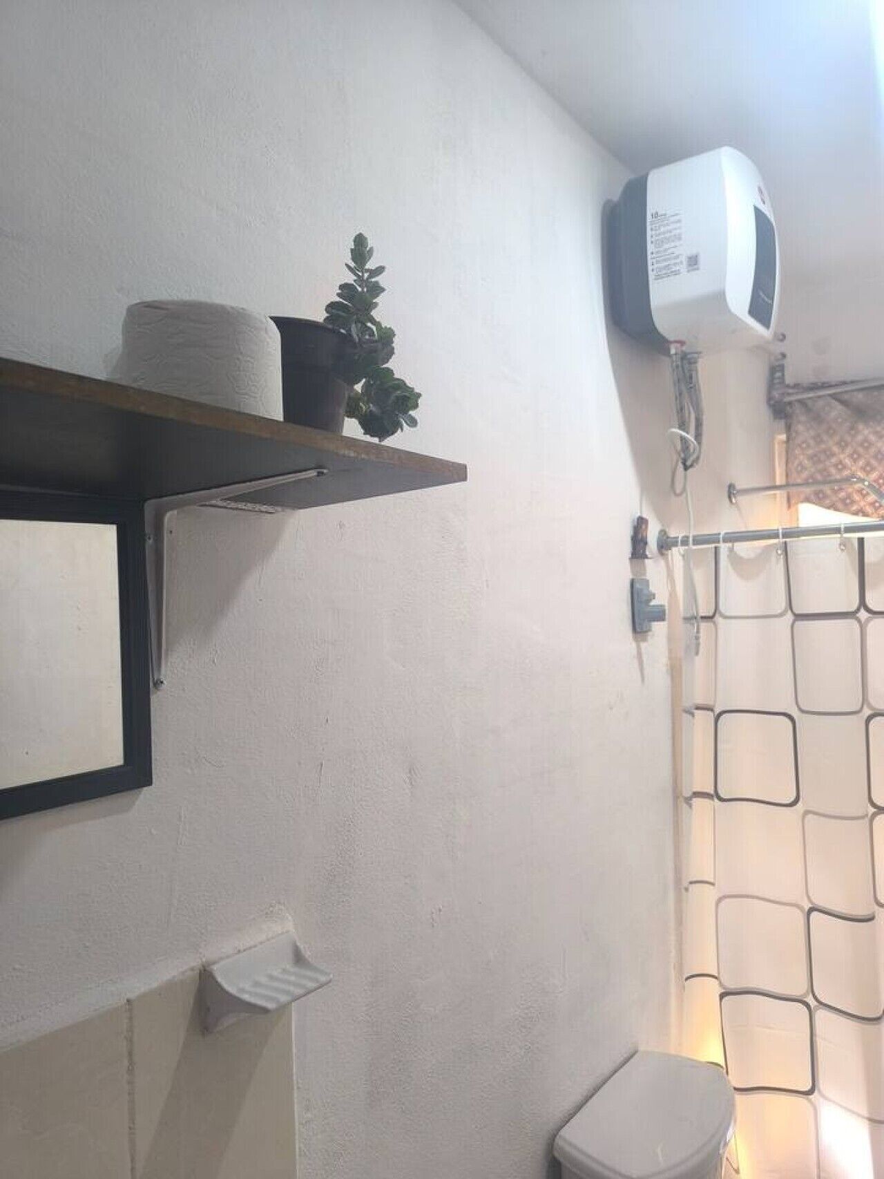 Et badeværelse med toilet, en hylde med toiletpapir, en potteplante, en bruseforhæng og en hårtørrer.
