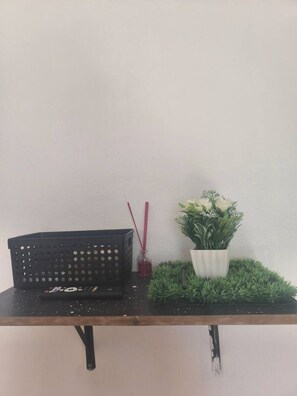 Une étagère avec un panier noir, un diffuseur de parfum en roseau rouge et un pot blanc contenant des plantes vertes.
