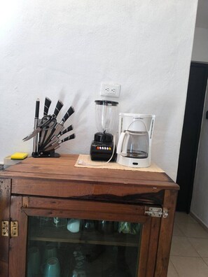 Een keukenhoek met een koffiezetapparaat, blender en messenstel op een houten aanrecht.