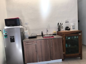 A compact kitchen with a refrigerator, microwave, sink, and a cabinet with glass doors.