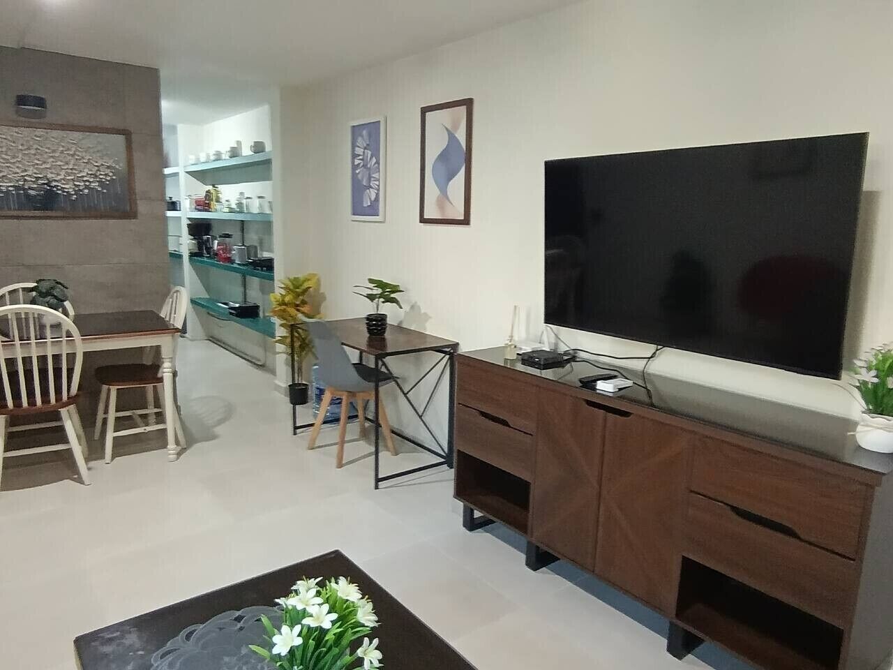 Un salon avec un téléviseur, des meubles en bois, un coin repas et une cuisine à l’arrière-plan.