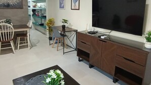 Una sala de estar con televisión, muebles de madera, un comedor y una cocina al fondo.