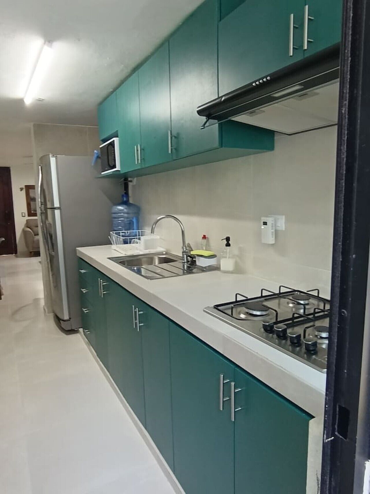 A kitchen with teal cabinets, a stainless steel refrigerator, a microwave, a sink, and a gas stove.