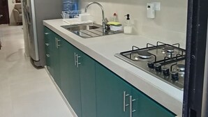 Una cocina con armarios color esmeralda, un refrigerador de acero inoxidable, un microondas, un lavamanos y una estufa a gas.