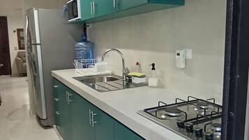 A kitchen with teal cabinets, a stainless steel refrigerator, a microwave, a sink, and a gas stove.