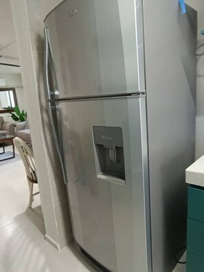 Ein Edelstahl-Kühlschrank mit Wasserspender in einer modernen Küche, mit weißen Schränken und einem Essbereich im Hintergrund.