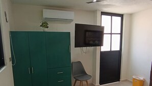 Un dormitorio con cama, un armario verde, una silla, un televisor y una ventana.