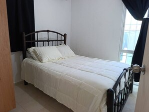 A single bed with a headboard, white bedding, and a door with a handle.