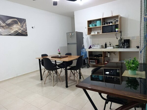 Ein Essbereich mit Tisch und Stühlen, inklusive Kühlschrank, Mikrowelle und einer Küchenzeile mit Utensilien.
