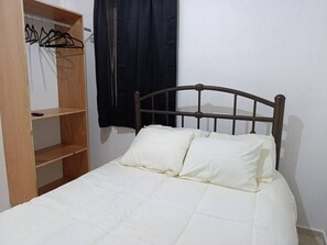 Ein Einzelbett mit Holz Kopfteil, ein Holzschrank und ein schwarzer Vorhang.