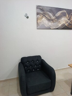 A black armchair in a room with a plain white wall and a single abstract painting.