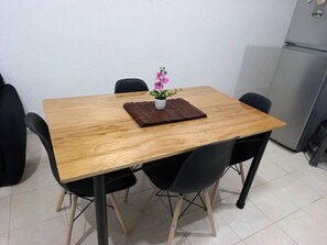 Een houten eettafel met vier zwarte stoelen, een kleine potplant en een koelkast op de achtergrond.
