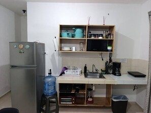 Een praktische keuken met een koelkast, magnetron, spoelbak en een klein aanrecht.