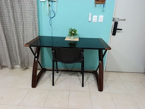 Ein Zimmer mit einer türkisfarbenen Wand, einem Glastisch, einem schwarzen Stuhl, einem kleinen Topfpflanzen und einer Tür mit Griff.