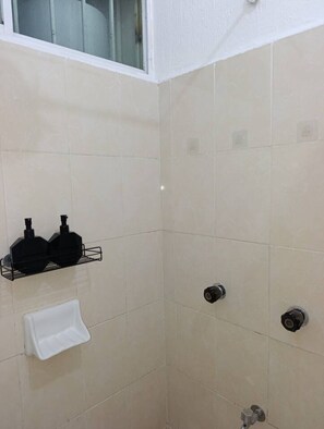 Ein Badezimmer im Eckbereich mit beigen Fliesen, einem Fenster, einem Handtuchhalter und zwei schwarzen Seifenspendern.