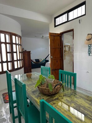 A dining area with a glass table, teal chairs, a woven basket with plants, and a wooden door. - Disfruta Chicxulub/2 Recamaras/4 personas (Chicxulub)
