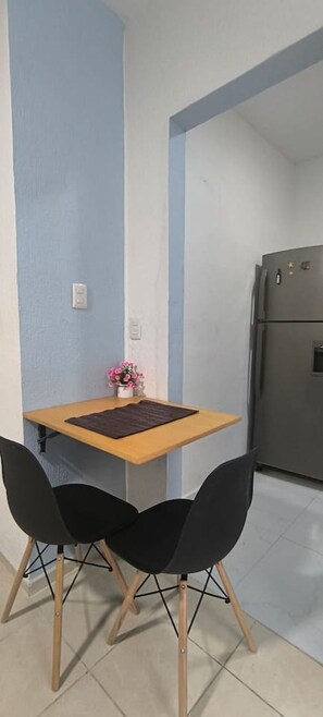 A small kitchen with a table and two chairs, a refrigerator, and a flower vase on the table. - Loft acogedor y funcional Facturamos (Merida)