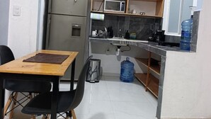 A compact kitchen with a refrigerator, microwave, and sink. There is a dining table with chairs, a water dispenser, and a trash can. - Loft acogedor y funcional Facturamos (Merida)