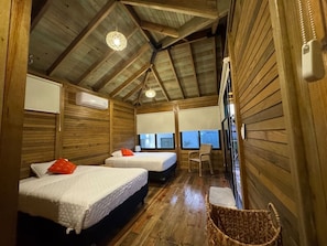 A wooden cabin with two beds, a chair, a small table, and a window with a view.